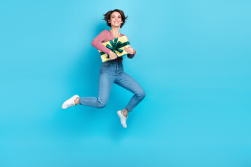 Full body photo of carefree energetic lady hands hold giftbox jumping empty space isolated on blue color background