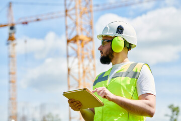 Construction worker or inspector engineer with tablet on building site in protecting sefety equipment - 605322135