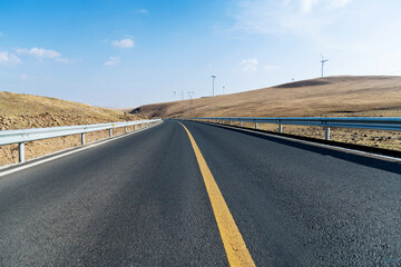 Empty asphalt highway road surrounded by fields with windmills