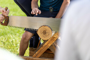 Un homme est assis sur un rondin de bois, et des personnes coupe le bois avec une scie