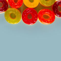 Some jelly sweets lie on plain light blue background. Delicious rounds arranged at the border of pic