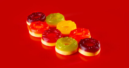Eight round jelly candies lie on red background. Delicious rounds arranged in diferent colors