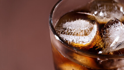 A glass of cola drink with ice cubes. Fresh cold sweet cola drink with ice one brown background with copy space.