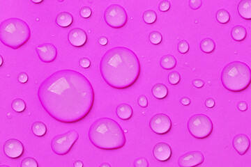 Water drops on pink background top view. Cosmetic moisturizing liquid drops of toner or hyaluronic serum.