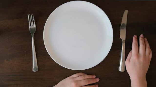 Hands in front of an empty white plate, fork and knife. Waiting gesture