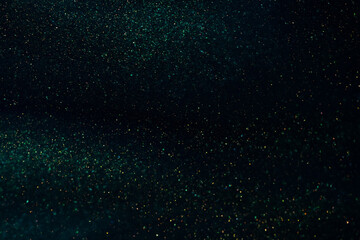 Abstract strains of gold particles in a green liquid. A dark mysterious glistening fluid background. Golden glittering particles on dark green-blue background.