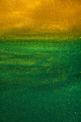Various stains and overflows of gold particles in two tones colored liquid. Beautiful galaxy of flying shiny golden particles on a green with yellow background. Magic golden dust particles with bokeh.