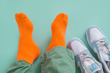 The feet of a man in orange socks with his sneakers take off. Mint green background.