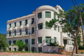 Fototapeta premium A low-rise deserted 1930s hotel with a decayed facade and green wooden window shutters under the summer blue sky.