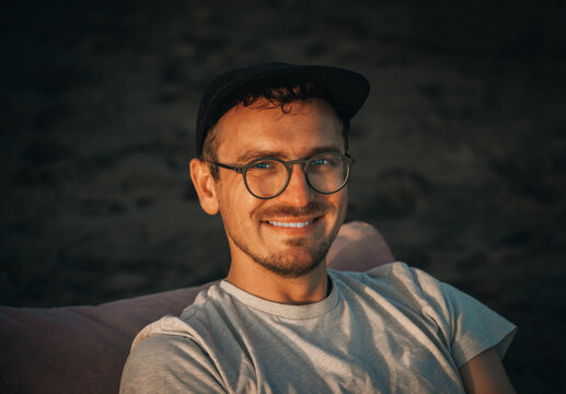 Young 32 years old Caucasian man traveler tourist with basecap on sandy beach on sand dune. Close-up summer headshot lifestyle portrait, three quarter portrait. Vacation, resting, relaxing.