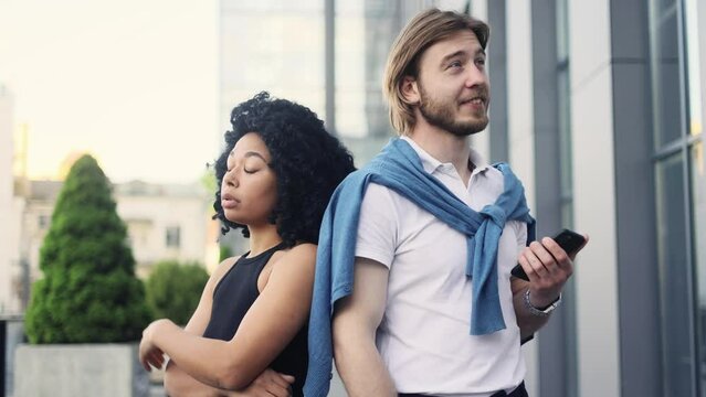 Narcissistic handsome young man gives an inspired introduction to his companion on date while she boring and rolls her eyes at city street Interracial people met after texting on dating app outdoors 