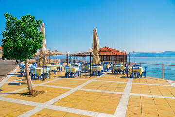 Empty tavern restaurant by the seafront with wooden chairs and tables under a bright sun in summer.