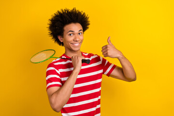 Photo of funny confident guy dressed red t-shirt playing badminton showing thumb up isolated yellow...