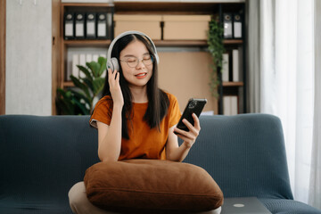 Smiling girl relaxing at home, she is playing music using smartphone tablet, laptop, and wearing white headphones. on sofa.