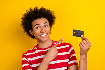 Photo of handsome guy indicate finger arm hold demonstrate debit card isolated on yellow color background