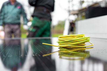 A coil of electric cable on a solar panel with technicians in the background