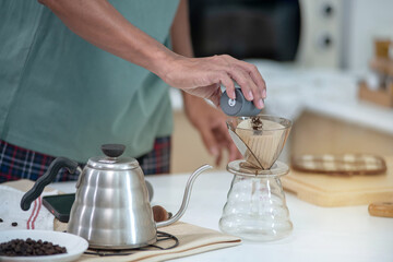 Man's hand was pouring lightly roasted and ground coffee onto the dripper, preparing coffee, Barista at home