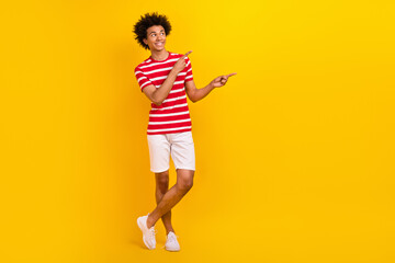 Full length photo of cute dreamy guy dressed red t-shirt pointing two fingers empty space isolated yellow color background
