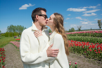 Guy and girl are kissing and hugs at field of colorful tulips.