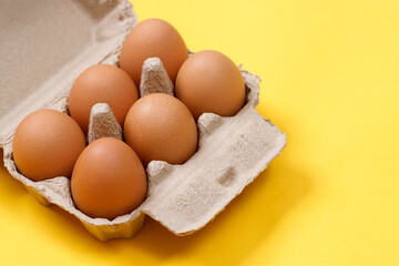 Chicken eggs in a cardboard box ready to cook on a yellow background