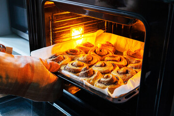 Baker wearing protective glove and checking her cinnamon rolls in the oven