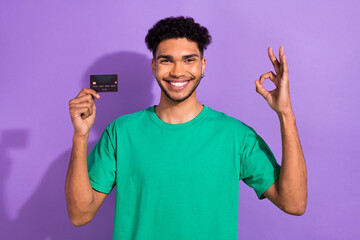 Photo of attractive charming man wear green t-shirt rising bank card showing okey isolated purple color background