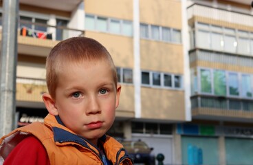 A short-haired blond boy looks thoughtfully into the distance. Perplexed six-year-old boy.