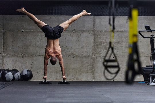 A muscular man in a handstand position, showcasing his exceptional balance and body control while performing a variety of exercises to enhance his overall body stability and strength in a modern gym