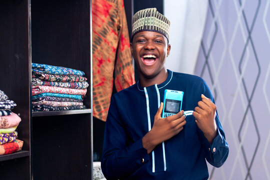 African Man Selling In A Fashion Market Using A Point On Sale Machine And Smiling. Payment Method, Cashless Transaction