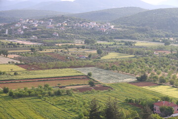 Naklejka premium Turkish village, fields and road on the mountain slope on a cloudy day. Agricultural landscape, fields and outbuildings, Mugla, Turkey, May 2023.