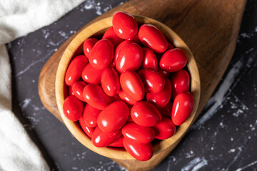 Chocolate almond dragee. Red chocolate dragee in wooden bowl on dark background. Top view
