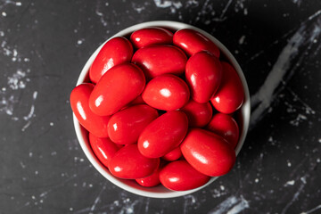 Chocolate almond dragee. Red chocolate dragee in ceramic bowl on dark background. Top view