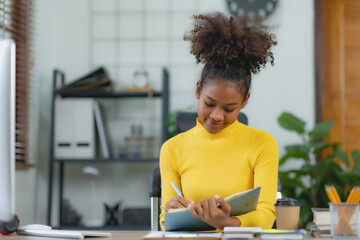 Beautiful young black woman using laptop computer at home. Young woman curly hair working on laptop and take note at home.