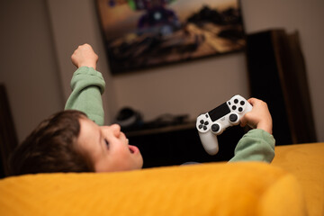 A little boy plays games on a game console with a gray joystick © volkonskaya
