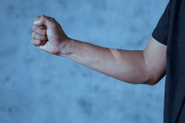 A man putting a plaster on his arm against an abstract light blue background