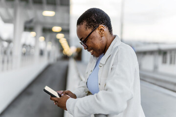 Woman waiting on a train station platform and using smartphone.