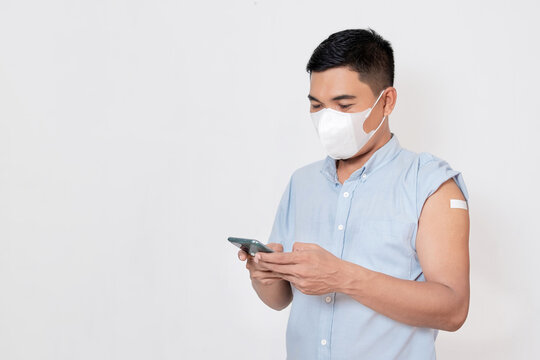 A vaccinated Asian adult man with a plaster bandage on his arm is checking data on a smartphone app. Protection against viruses.