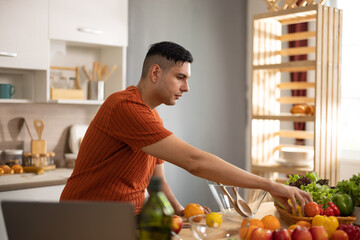 A homely and healthy male prepares nutritious diet, including variety of fruits. Following cooking show on laptop Mastery of peeling, chopping, and slicing fruits to prepare them in artistic style.