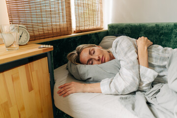 Attractive caucasian sleeping woman. Clock and pills on the nightstand next to the bed.