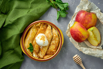 Pancake rolls stuffed with apple and sour cream in a clay bowl on a gray background. Blini, stuffed crepe