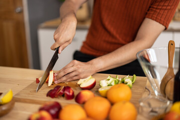 A homely and healthy male prepares nutritious diet, including variety of fruits. Following cooking show on laptop Mastery of peeling, chopping, and slicing fruits to prepare them in artistic style.