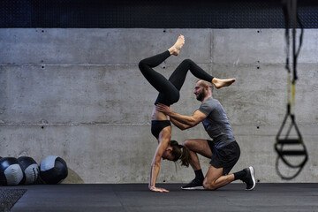 A muscular man assisting a fit woman in a modern gym as they engage in various body exercises and muscle stretches, showcasing their dedication to fitness and benefiting from teamwork and support