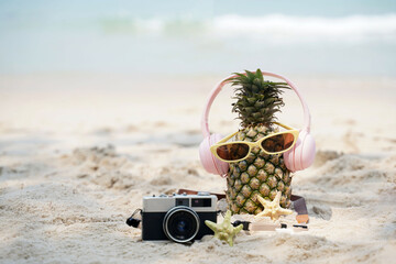 Summer party. Pineapple wearing sunglasses and listen to music on beach and blue sky background. Tropical fashion. Summer Fashion on holiday concept.