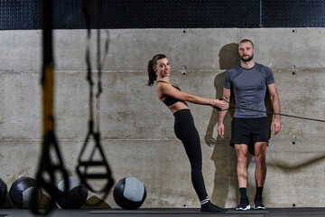 A muscular man assisting a fit woman in a modern gym as they engage in various body exercises and muscle stretches, showcasing their dedication to fitness and benefiting from teamwork and support