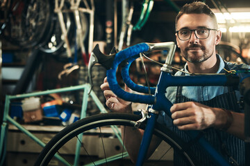 Obraz na płótnie Canvas Portrait, serious and repair man in bicycle shop working in store and cycling workshop. Face, bike mechanic and confident male person, professional and mature technician from Canada with glasses.