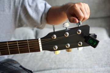 Selected focus photo of someone tuning guitar with digital guitar tuner.                   