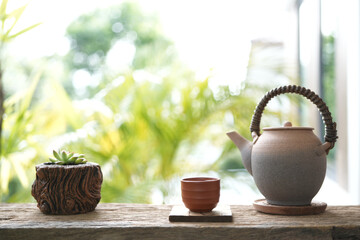 Tea cup and cactus pot and old tea pot on wooden table with notebook