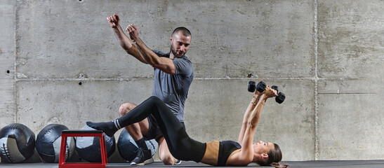 A muscular man assisting a fit woman in a modern gym as they engage in various body exercises and muscle stretches, showcasing their dedication to fitness and benefiting from teamwork and support
