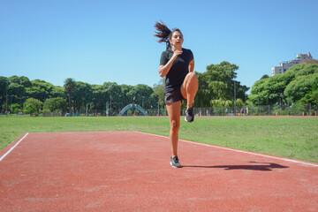 young latin woman warming up on the running track with jumps and bent leg raises