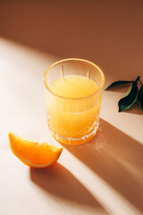 Orange juice on beige table with long shadows. Healthy drink. Closeup